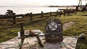 Ein Picknick mit Korb, Weinflasche und Gläsern auf einer Decke am Seeufer.