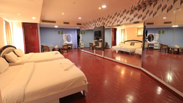 A hotel room with two beds, a large mirror, a TV, and a bathroom with a toilet and sink. - Aishwaryam Hotel (Madurai)