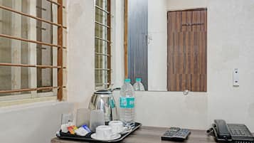 A hotel room with a window, a wooden door, a tray with water bottles, cups, and a kettle.