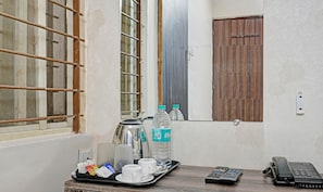 A hotel room with a window, a wooden door, a tray with water bottles, cups, and a kettle.
