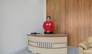 A reception desk with a wooden panel wall, a beige counter with metal handles, and a chair to the right. - Treebo Alankar Hoshangabad Road (Bhopal)