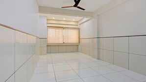 A spacious hallway with white tiled floors and walls, a ceiling fan, and a window with blinds. - Treebo Alankar Hoshangabad Road (Bhopal)