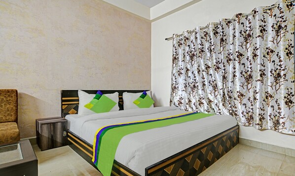 A bedroom with a bed, a nightstand, a chair, and a window with curtains.