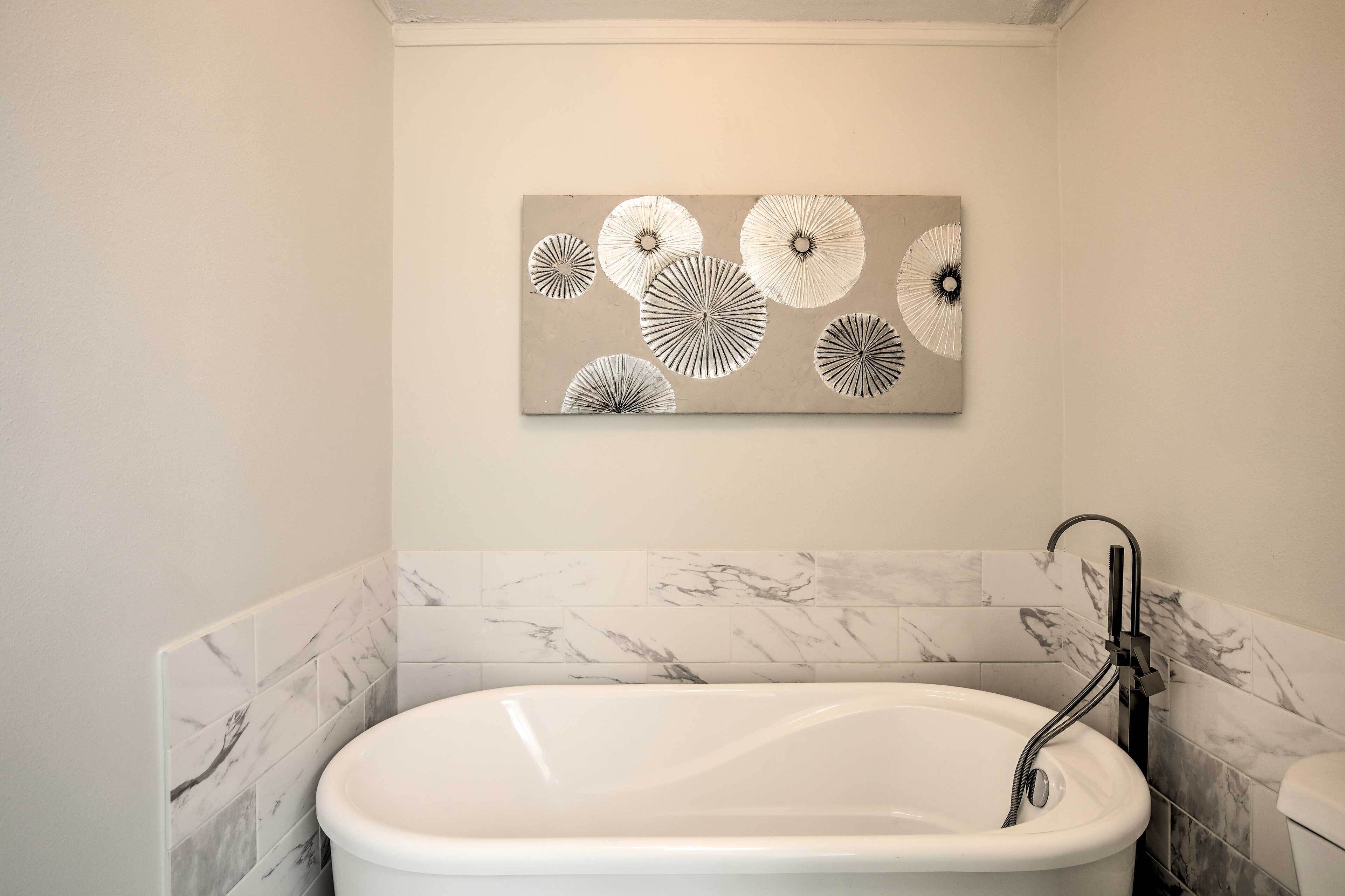 A bathroom with a freestanding bathtub, marble tiles, and a wall-mounted abstract art piece.