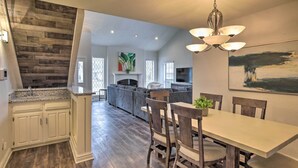 A spacious kitchen with a wooden accent wall, a dining area with a table and chairs, and a living room with a gray sofa and fireplace. - Game Room & Private Pool: Richardson Retreat (Richardson)