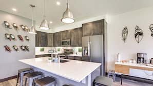 Une cuisine moderne dotée d’un grand îlot central, d’appareils électroménagers en acier inoxydable et de luminaires suspendus.