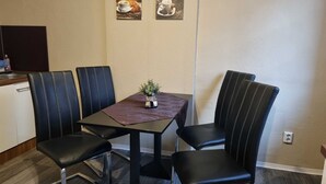Ruokailutilassa on pöytä ja neljä tuolia, pöydällä on pieni kasvi ja seinällä kaksi kehystettyä kuvaa.