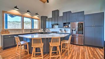 A modern kitchen with a large island, grey cabinets, stainless steel appliances, and wooden bar stools.