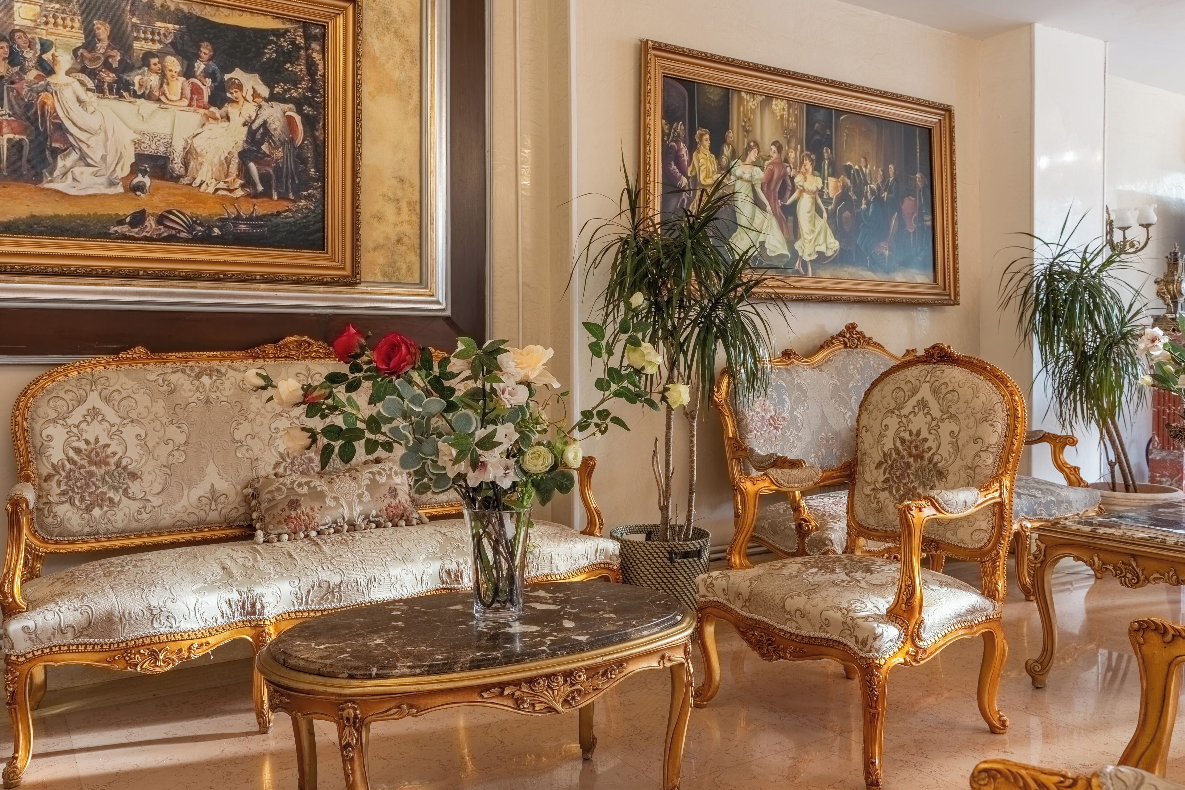 Une chambre luxueuse, meublée avec goût, comprenant un canapé et des fauteuils, une table basse en marbre et deux tableaux accrochés aux murs.