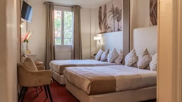 Quarto de hotel com duas camas, uma escrivaninha, televisão e janela com cortinas.