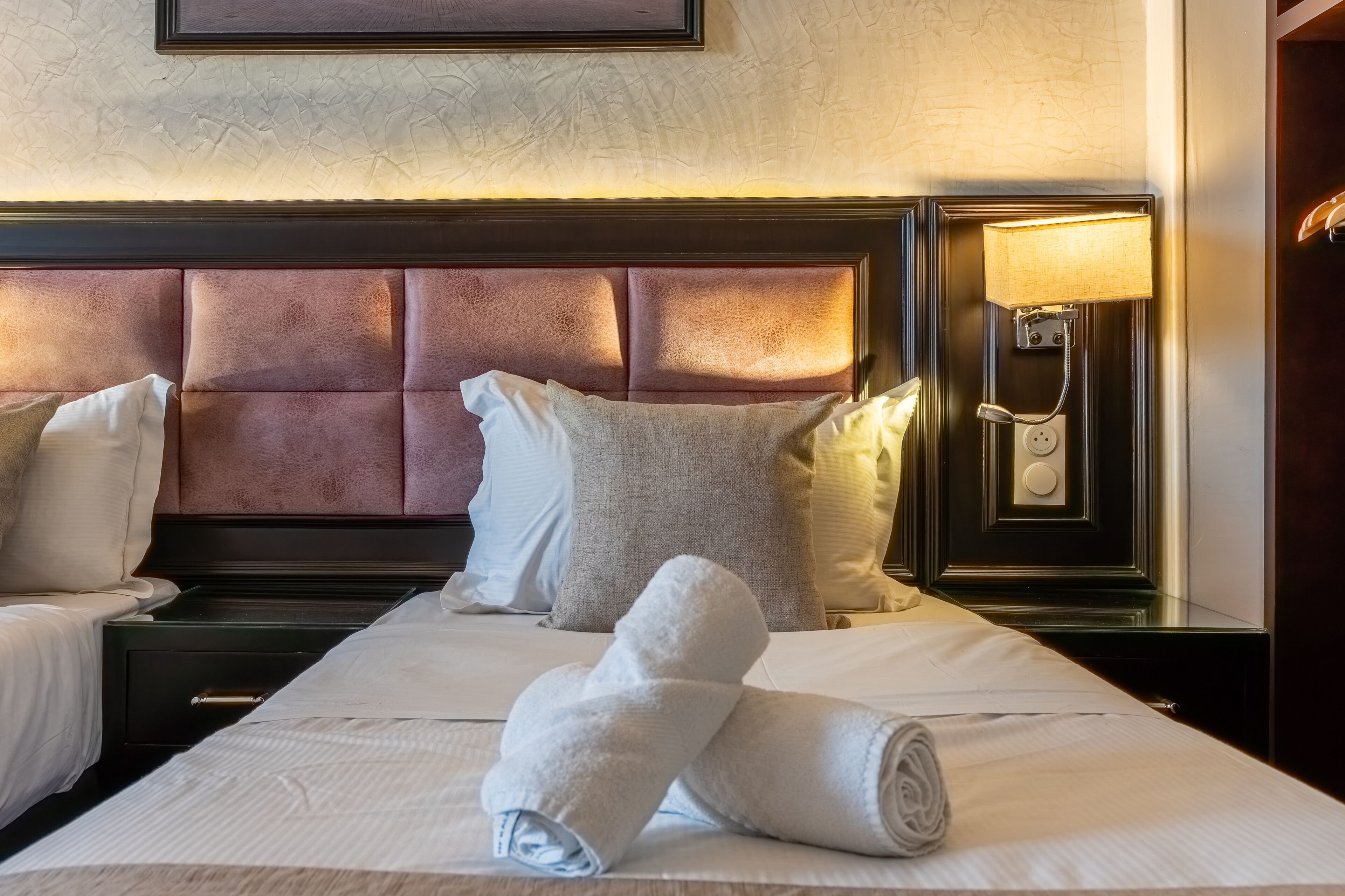 A hotel room with a large bed, two bedside tables, a headboard, and a wall-mounted lamp.