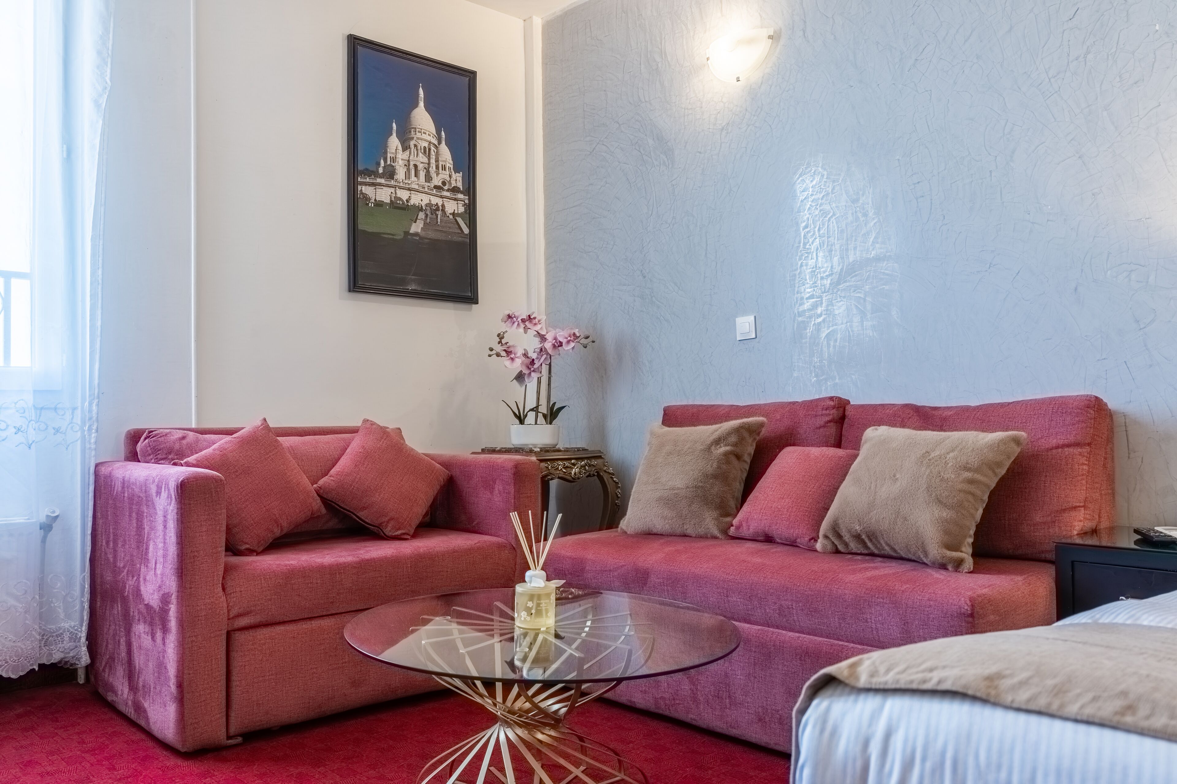 A room with a red sofa, a glass coffee table, a framed picture on the wall, and a small side table with a plant.