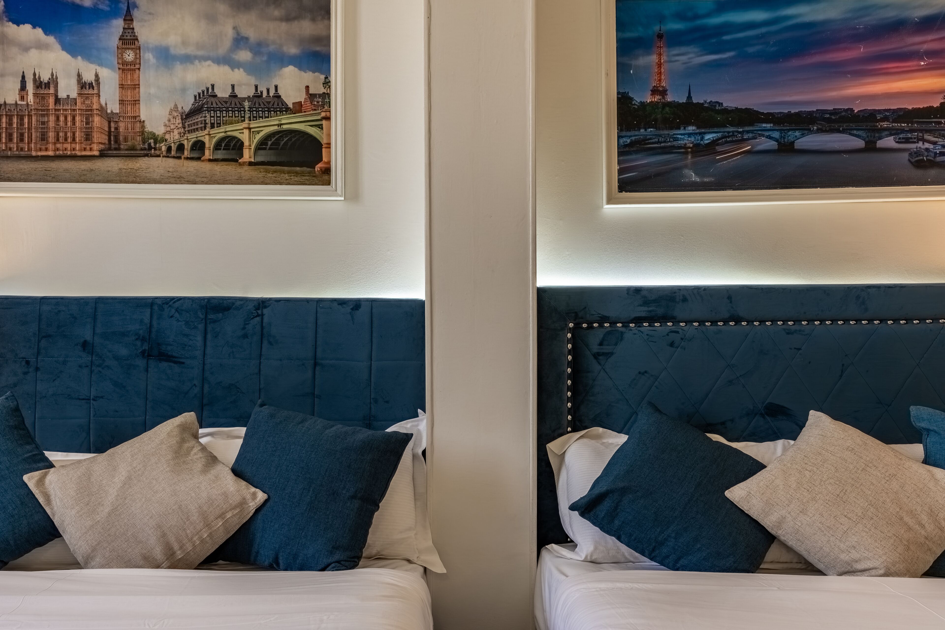 Twee bedden met hoofdeinden, een schilderij van een stadsgezicht en uitzicht op een nachthemel.
