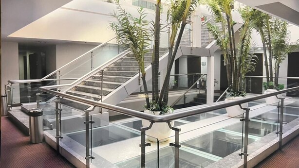 En moderne indendørs atrium med glasgelændere, en central trappe og plantekasser.