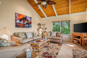A living room with a wooden ceiling, a large painting of a volcano, a sofa set, a coffee table, and a TV stand.