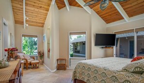 Ein Schlafzimmer mit einem großen Bett, einem an der Wand befestigten Fernseher und einer Balkontür, die zu einem Außenbereich führt.