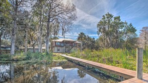 A house with a wooden deck over a pond, surrounded by trees and vegetation. - Waterfront Home w/ Private Dock in Crystal River (Crystal River)