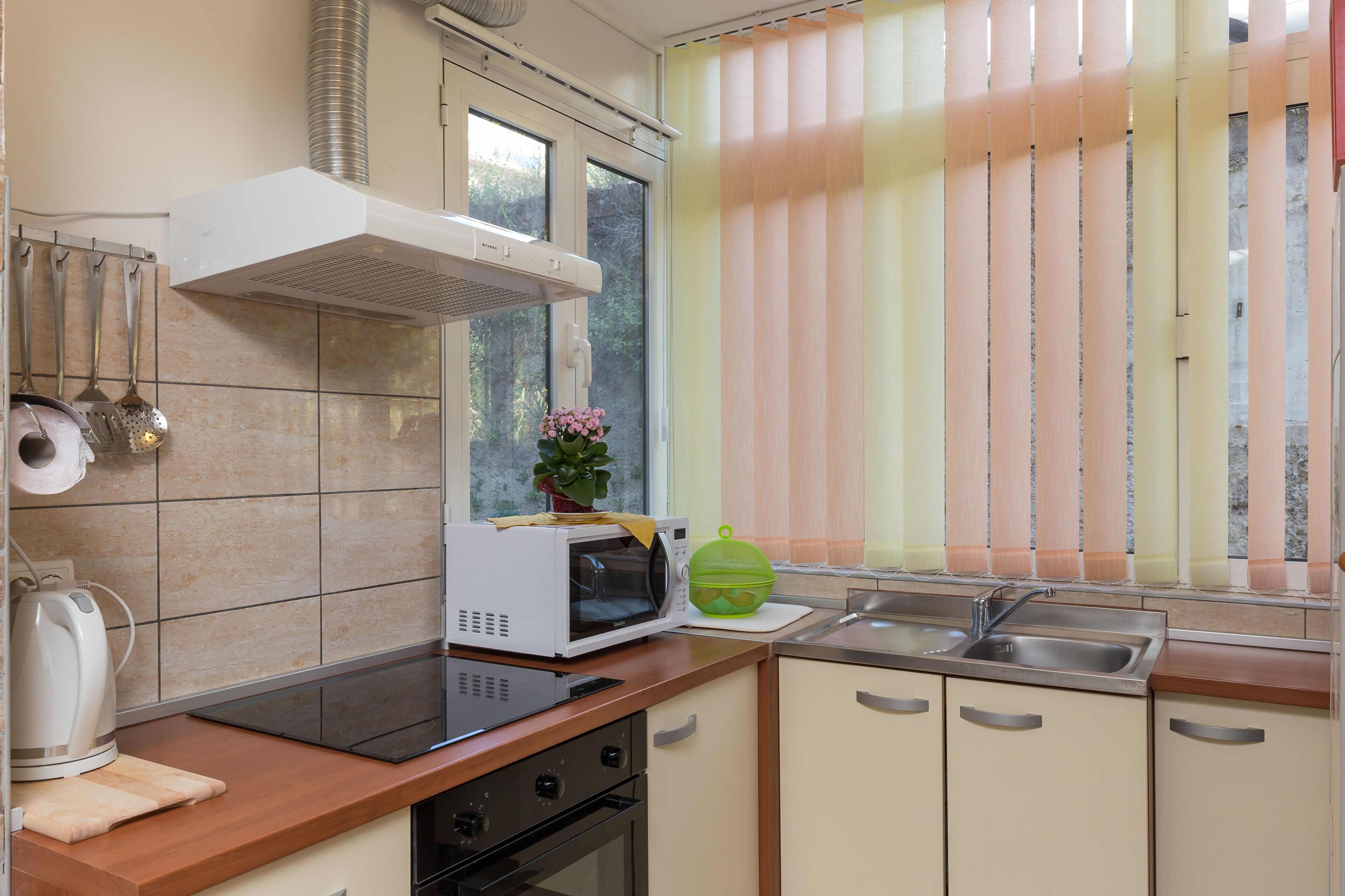 A kitchen with a microwave, stove, sink, and hanging utensils.