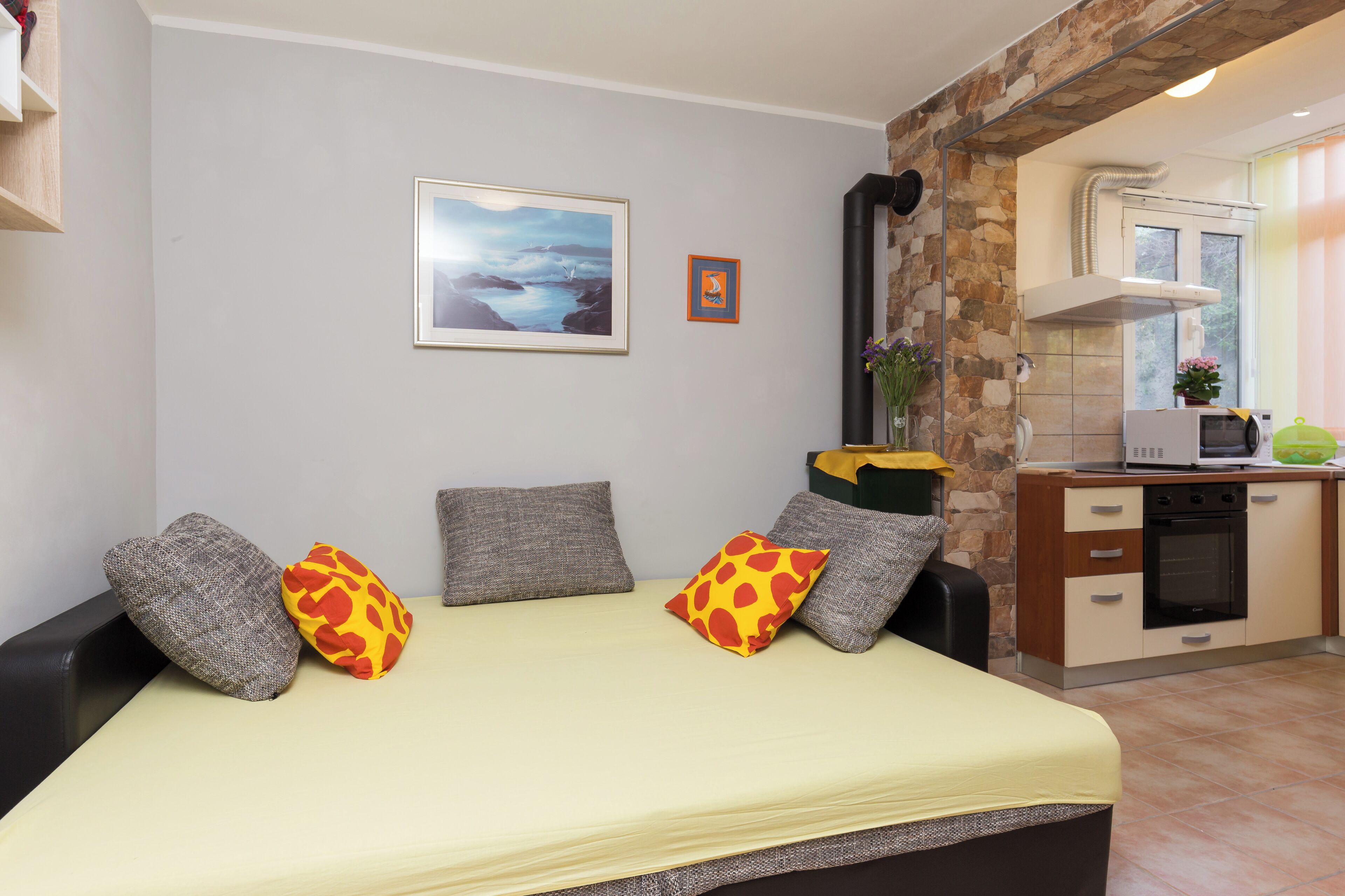 Un dormitorio con cama, almohadas, un cuadro enmarcado y una zona de cocina con electrodomésticos.
