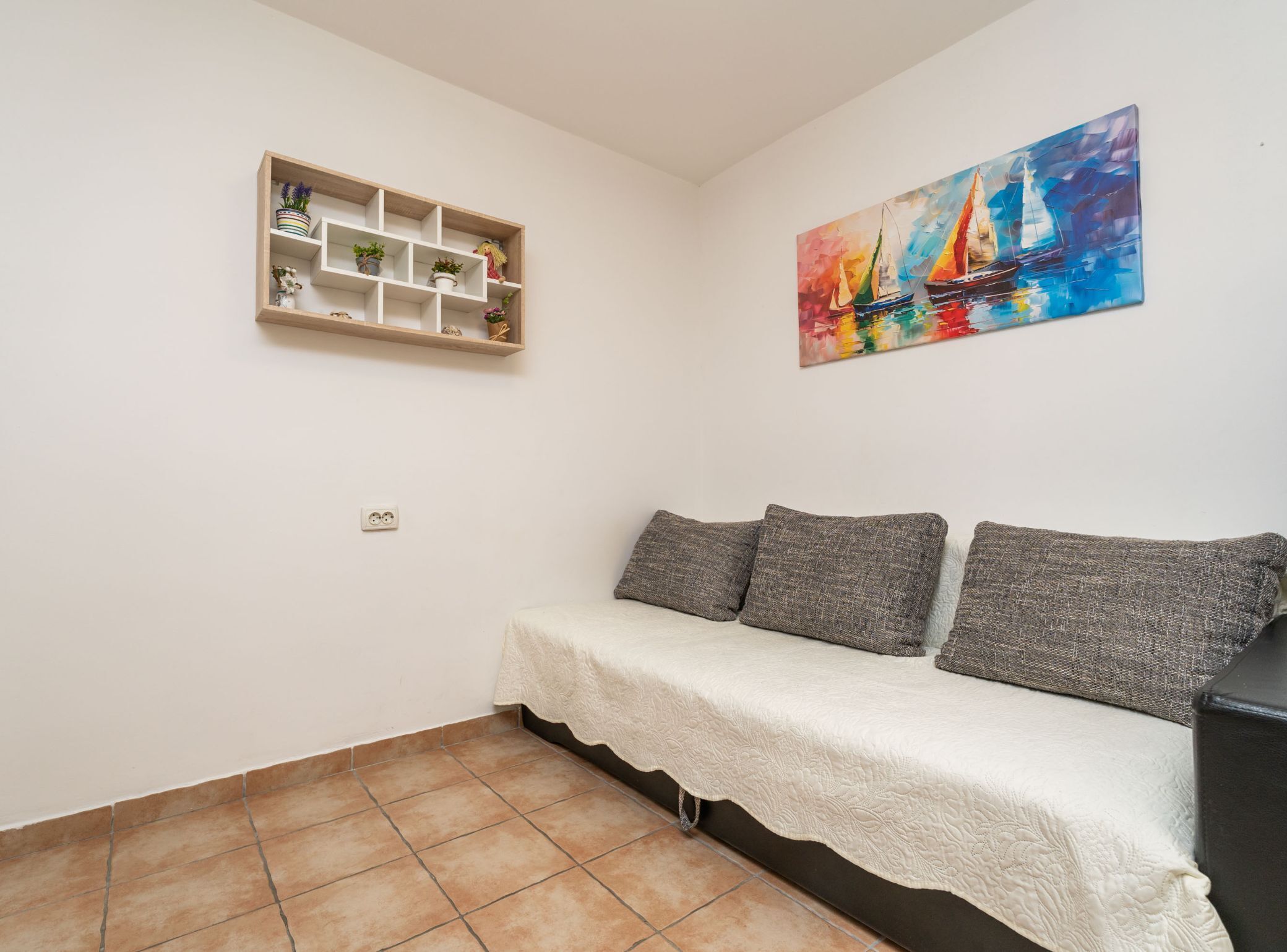 Un pequeño espacio de estar con un sofá, una estantería con plantas y un cuadro de colores en la pared.
