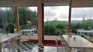 A dining area with checkered flooring, white tables and chairs, and large windows offering a view of greenery and hills. - Belvilla by OYO Hotel Alimunera (Naso)
