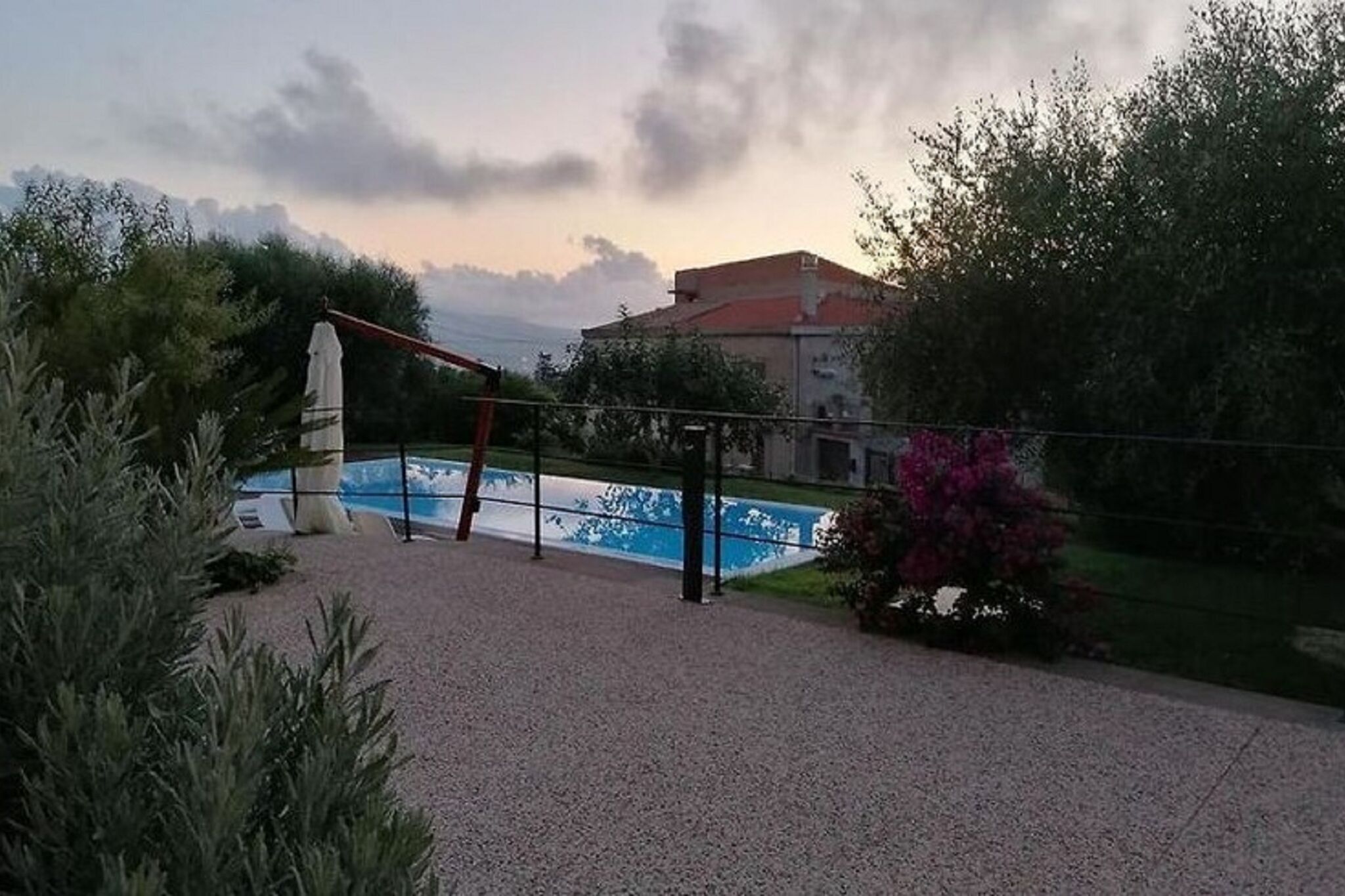 Área de piscina com uma estátua, rodeada por cascalho e vegetação, com um edifício ao fundo.