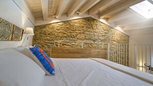 A bedroom with a stone wall, wooden beams, a bed with white bedding, and a skylight. - Belvilla by OYO Hotel Alimunera (Naso)
