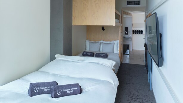 A hotel room with a bed, pillows, a wooden headboard, a TV, and a small bathroom area. - Sakura Cross Hotel Uenoiriya Annex (Tokyo)