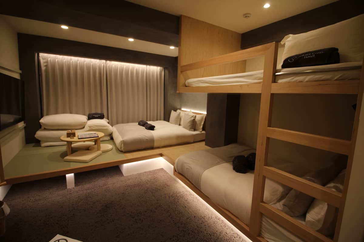 A bunk bed room with a desk, pillows, and a window with curtains.