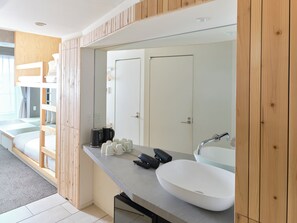 A modern bathroom with a large mirror, a white sink, and a built-in bench with storage.