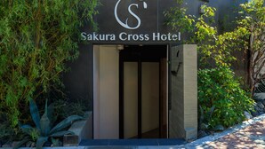 The entrance to Sakura Cross Hotel with a modern design, featuring a logo above the entrance and a pathway leading to the door.