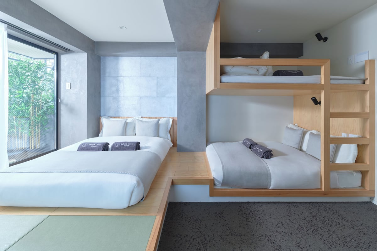 A modern hotel room with a large bed, a lower bunk bed, and a built-in desk.