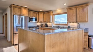 A modern kitchen with wooden cabinets, stainless steel appliances, granite countertops, and a large window offering a view.