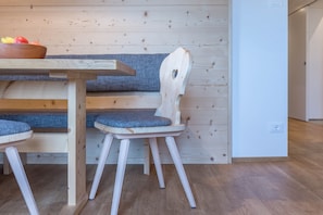 Une table de salle à manger en bois, sur laquelle se trouve un saladier rempli de fruits, un banc bleu avec un coussin et une chaise en bois dotée d’un motif ajouré.