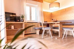Une pièce confortable, aménagée comme un chalet, avec un intérieur en bois, une table à manger avec des chaises, un téléviseur et une fenêtre avec des rideaux.