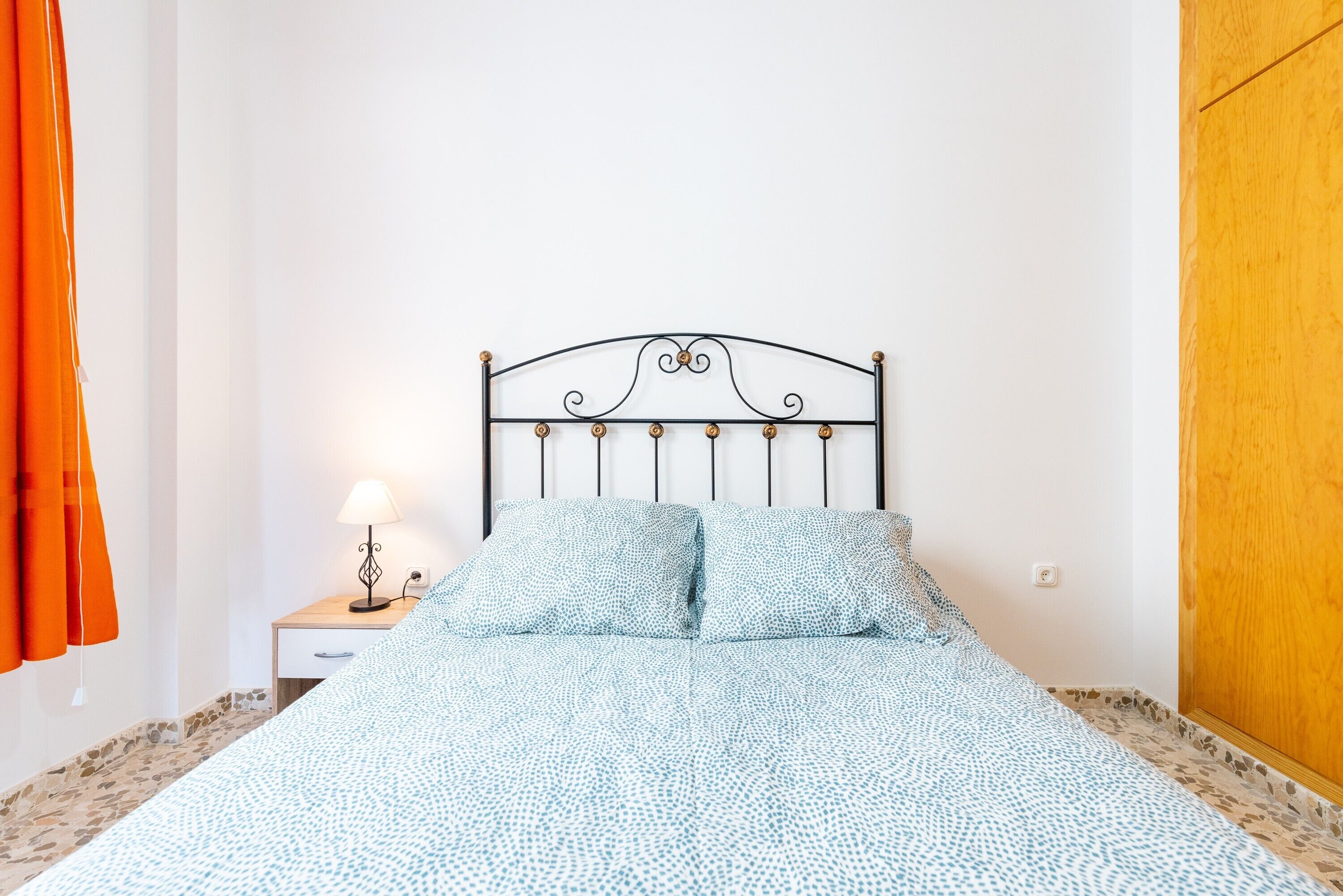 Ein Schlafzimmer mit einem Bett, einem Nachttisch, einer Lampe und einer Holztür.
