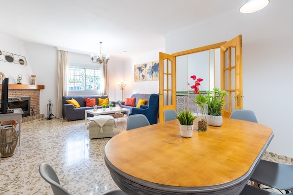 Ein modernes Wohnzimmer mit Kamin, Esstisch mit Stühlen, einer Couch mit Kissen und einem großen Fenster.