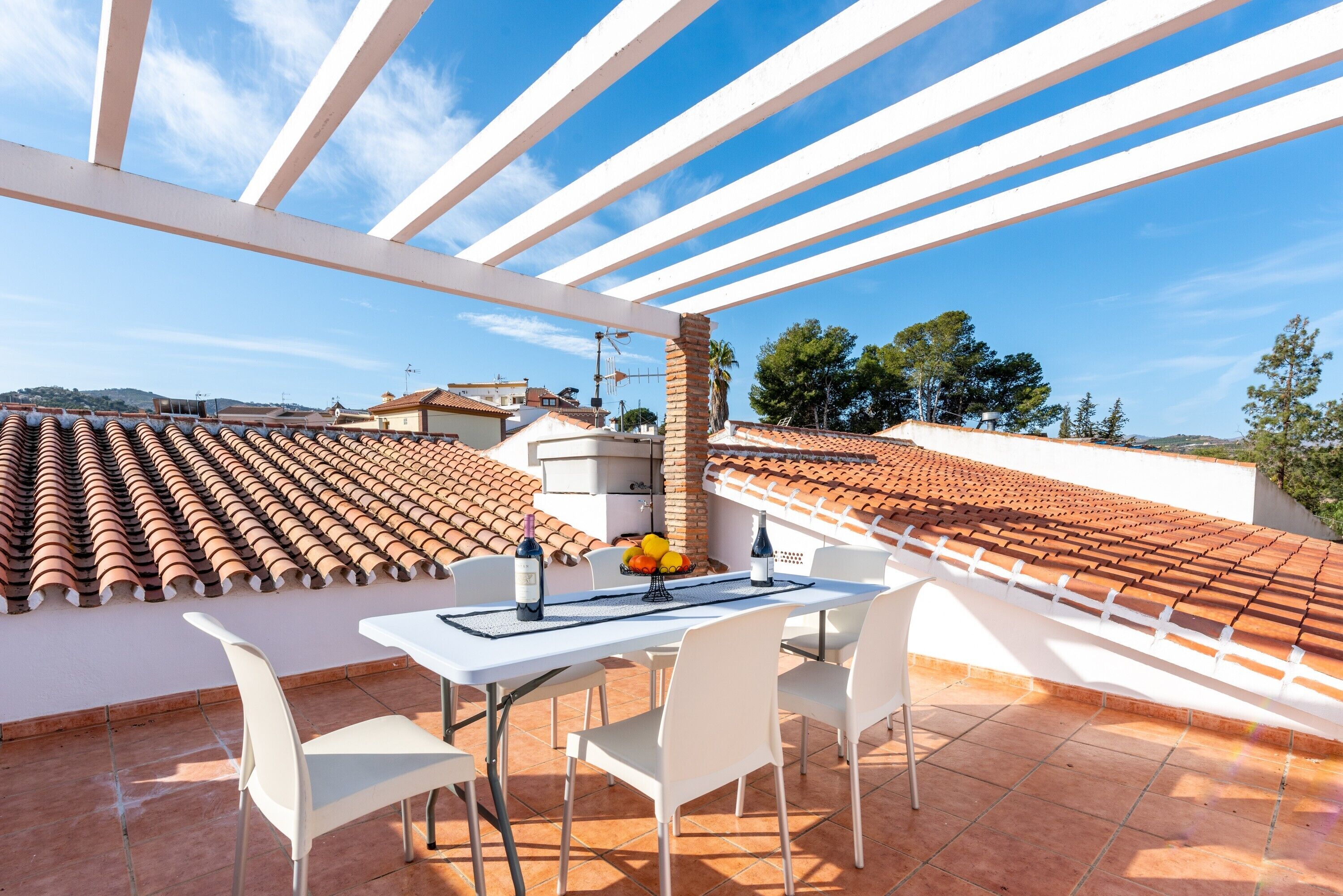 Una terrazza con tavolo e sedie, una bottiglia di vino e una ciotola di frutta.