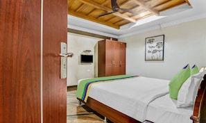 A hotel room with a wooden ceiling, a bed with a colorful bedspread, a wardrobe, a wall-mounted TV, and a framed floral artwork. - Treebo Symphony Hotels And Resorts Angamally (Chalakudy)