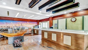 A reception area with a wooden reception desk, a clock, a reception sign, a fan, and a decorative wall with a sunset mural. - Treebo Symphony Hotels And Resorts Angamally (Chalakudy)