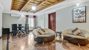 A modern living room with a marble floor, two sofas, a dining area with a table and chairs, a wooden ceiling, and a painting on the wall. - Treebo Symphony Hotels And Resorts Angamally (Chalakudy)