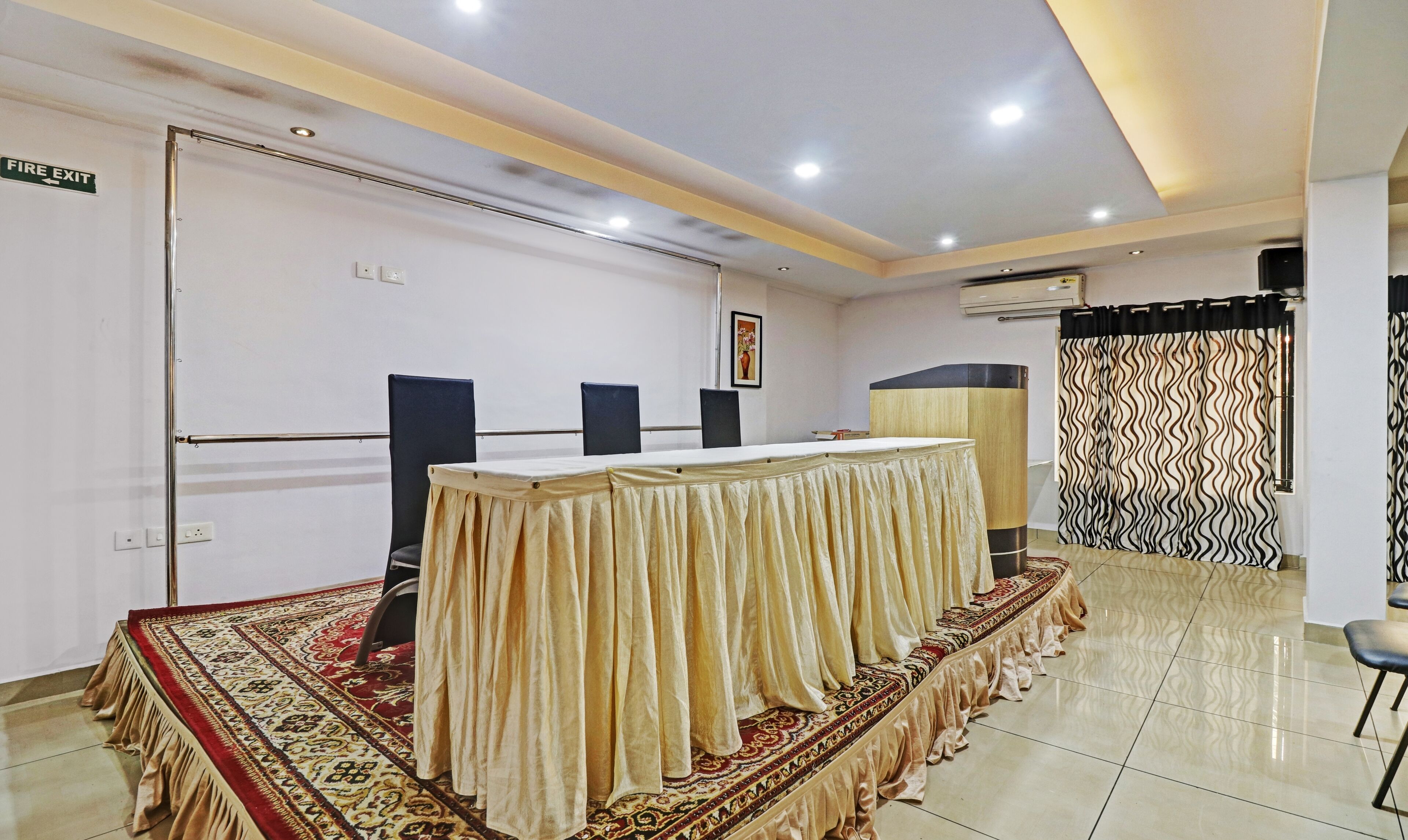 A conference room with a long table, chairs, a fire exit sign, and a patterned curtain.