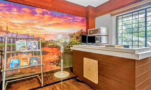A reception area with a large mural, a fan, a coffee machine, and a window with a view of greenery. - Treebo Symphony Hotels And Resorts Angamally (Chalakudy)