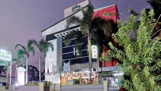 A modern hotel with a glass facade, palm trees, and a sign for Symphony Hotels & Resorts. - Treebo Symphony Hotels And Resorts Angamally (Chalakudy)