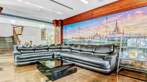 A modern living room with a sectional sofa, a glass coffee table, and a large mural of a temple. - Treebo Symphony Hotels And Resorts Angamally (Chalakudy)