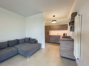 A modern kitchen with a built-in stove, a dining area with a table, and a grey sectional sofa.