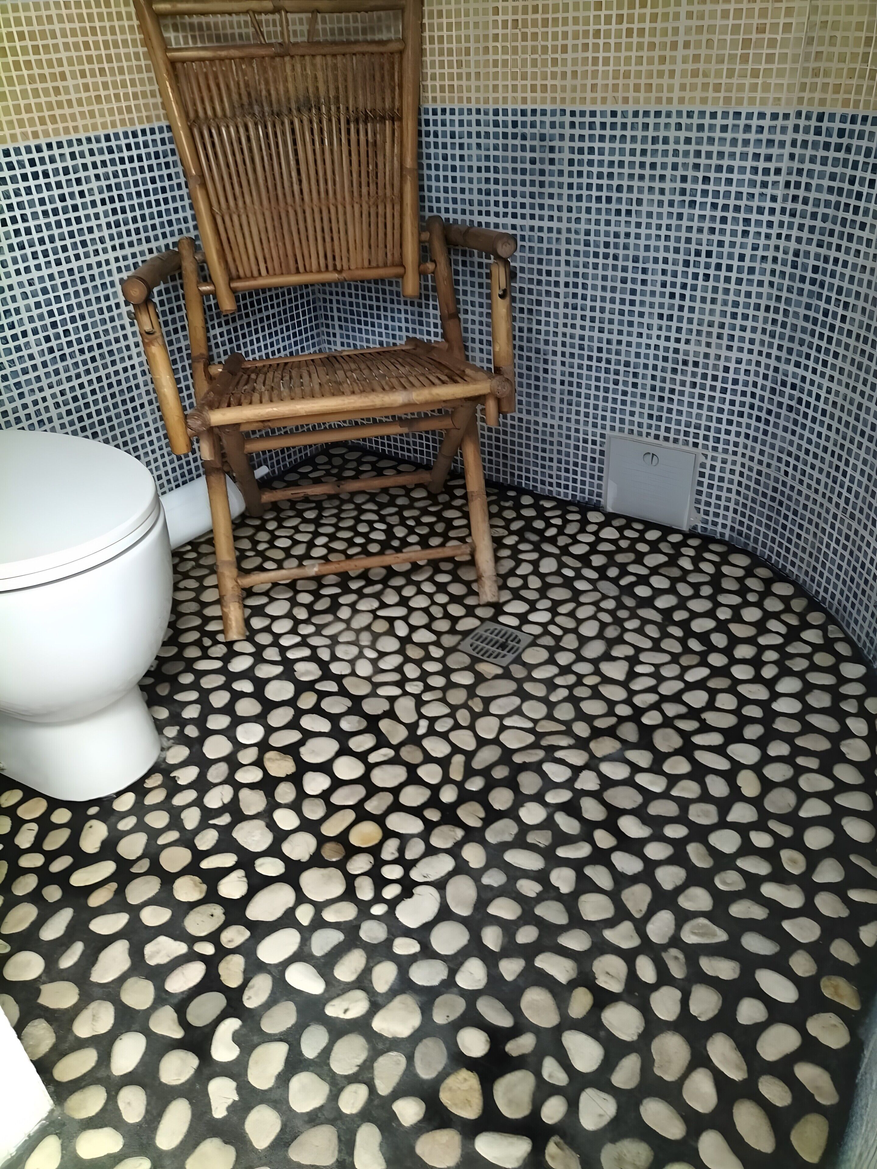A bathroom with a toilet, a wooden chair, and a floor with a pebble pattern.