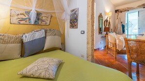 Ein Zimmer mit einem Bett, einem Sessel, einem Tisch und Bildern an den Wänden.