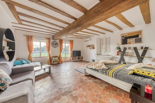 A spacious room with a large bed, a sofa, and a television. The room has a rustic ceiling with exposed beams and a tiled floor.