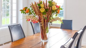 Ett matbord med en genomskinlig glasvas som innehåller blommor och pampasgräs.